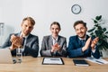 Smiling recruiters clapping and looking at camera near documents and laptop