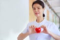 Smiling Red heart held by smiling female nurse`s hand in health care hospital or clinic. Professional, Specialist, Experienced