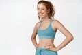 Smiling redhead sportswoman in sportsbra, hold hands on waist and looks happy doing sports. Fitness girl workout against