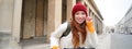 Smiling redhead woman stands near building, rents e-scooter to travel around town while on tourist trip Royalty Free Stock Photo