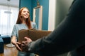 Smiling redhead young woman accepting cardboard box from unrecognizable delivery man on doorstep at apartment Royalty Free Stock Photo