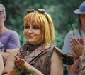 Smiling redhead young woman in leather costume claps hands at public fantasy festival