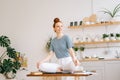 Smiling redhead young woman sitting in lotus pose at the desk and looking away. Royalty Free Stock Photo