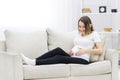 Smiling regnant woman put her hands on her stomach on white sofa. Royalty Free Stock Photo