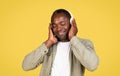 Smiling relaxed adult black guy in casual, wireless headphones enjoying music in free time