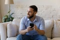 Smiling relaxed dreamy young man using smartphone at home.