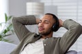 Smiling and relaxed hispanic man relaxing at home on sofa wearing headphones, listening to music, audiobook, podcast Royalty Free Stock Photo