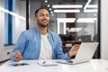 Smiling and relaxed young hispanic man sitting at desk in office in lotus position and meditating with closed eyes Royalty Free Stock Photo