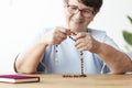 Smiling religious elderly woman praying with rosary at table wit