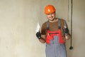 Smiling repairman in overalls and protective orange helmet holds two spatulas for plastering concrete wall with putty Royalty Free Stock Photo