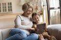Smiling retired nanny and little girl watch cartoon using tablet