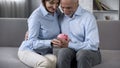 Smiling retiree couple sitting on couch holding piggy bank, crediting service