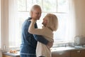 Smiling romantic aged couple dancing in kitchen