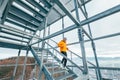 Smiling runner man dressed in bright orange softshell sporty clothes running down by huge steel industrial stairs in cold winter