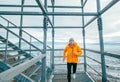 Smiling runner man dressed in bright orange softshell sporty clothes running down by huge steel industrial stairs in cold winter