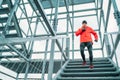 Smiling runner man dressed bright red softshell sporty clothes running down by huge steel industrial stairs in cold winter day.