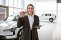 Smiling saleswoman giving to customer car key at new car showroom.
