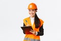 Smiling satisfied asian female construction engineer leading inspection at enterprise, wearing safety helmet and