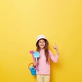 Smiling satisfied little cute girl in panama holding beach sandbox toys rake and shovel isolated over yellow background pointing Royalty Free Stock Photo