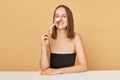 Smiling satisfied young brown haired woman wearing black top with makeup brushes in hand posing  over beige background Royalty Free Stock Photo