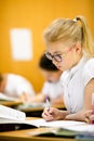 Smiling scholar girl sitting with other children in classroom and writing on textbook. Happy student doing homework at elementary Royalty Free Stock Photo