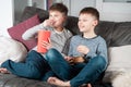 Smiling school aged boys sit on sofa, eat popcorn and watch comic TV show. Kids having fun and relaxing in home room. Royalty Free Stock Photo