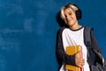 Smiling schoolboy in wireless headphones with textbooks and backpack