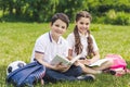 smiling schoolchildren doing homework together while sitting on grass in park and looking