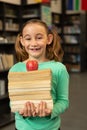 Smiling schoolgirl with books and apple standing in library