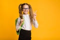 Smiling Schoolgirl Gesturing Victory Sign In Studio