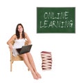 Smiling schoolgirl with a huge pile of books and a computer on her lap in front of a chalkboard Royalty Free Stock Photo