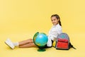 Smiling schoolgirl sitting near globe and