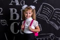 Smiling schoolgirl standing before the chalkboard as a background with a backpack on her back. Enlarged view