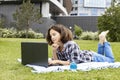 A smiling schoolgirl studies remotely. The girl uses wireless internet technologies. A pretty young teenage girl lies on the grass