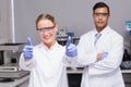 Smiling scientist looking at camera thumbs up with her colleague behind