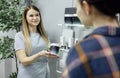 Smiling seller offers to choose the right cosmetics for female client. Plastic jar mockup in the hands of a seller woman