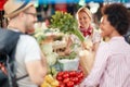 Smiling Seller woman offers fresh and organic vegetables at the green market or farmers market stall.  Young buyers choose and buy Royalty Free Stock Photo