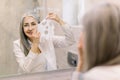 Smiling senior attractive woman is applying sheet mask on her face in the bathroom. Fabric cloth face mask to improve
