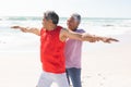 Smiling senior biracial woman helping man with arms outstretched yoga posture at sunny beach Royalty Free Stock Photo