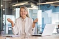 Smiling senior businesswoman sitting in the office at the desk in the lotus position with closed eyes, meditating Royalty Free Stock Photo