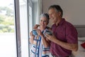 Smiling senior caucasian couple standing looking out of window embracing holding cups of coffee Royalty Free Stock Photo