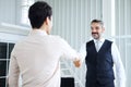 Smiling Senior Caucasian manager shaking hand with young Asain businessman after meeting and successful