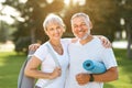 Smiling senior couple husband and wife embracing while standing at park with exercise mats Royalty Free Stock Photo