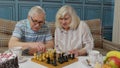 Smiling senior couple grandfather grandmother resting on sofa drinking coffee, playing chess at home Royalty Free Stock Photo