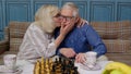 Smiling senior couple grandfather grandmother resting on sofa drinking coffee, playing chess at home Royalty Free Stock Photo