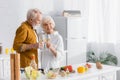 Smiling senior couple holding glasses of wine embracing near vegetables on blurred foreground. Royalty Free Stock Photo