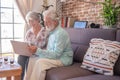 Smiling senior couple at home sitting on sofa using laptop computer.  Brick wall on background Royalty Free Stock Photo