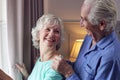 Smiling Senior Couple At Home Wearing Pyjamas Opening Bedroom Curtains And Looking Out Of Window