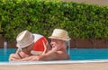 Smiling senior couple plays in the pool with an inflatable ball. Happy retirees enjoy summer holidays under the sun