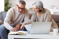 Smiling senior couple reading notification letter with good news from bank while sitting with laptop Royalty Free Stock Photo